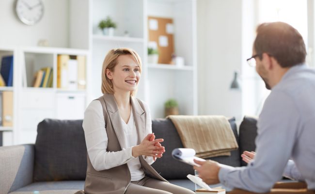 Young blonde smiling woman sitting on couch and looking at counselor during discussion of ways of solving problem
